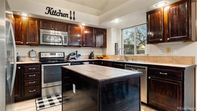 kitchen featuring tile counters, dark brown cabinets, stainless steel appliances, and a sink