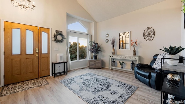 foyer entrance with a notable chandelier, light wood finished floors, and high vaulted ceiling