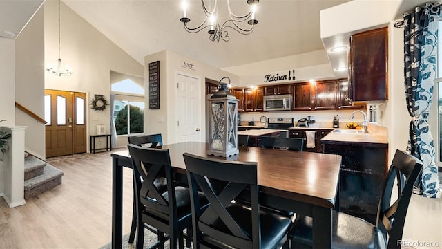 dining room featuring a notable chandelier, light wood-style flooring, stairs, and vaulted ceiling