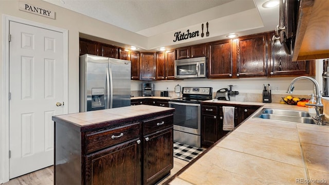 kitchen featuring a sink, a center island, tile countertops, stainless steel appliances, and dark brown cabinets