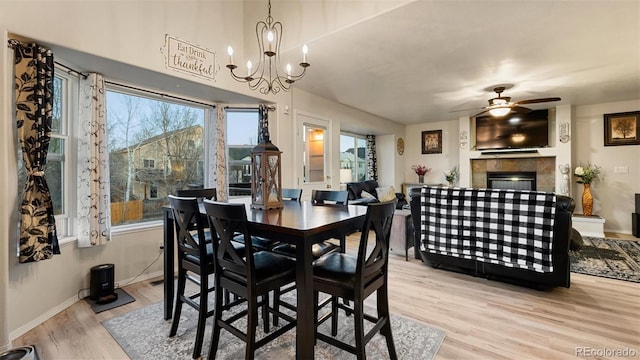 dining area with baseboards, ceiling fan with notable chandelier, wood finished floors, and a tile fireplace