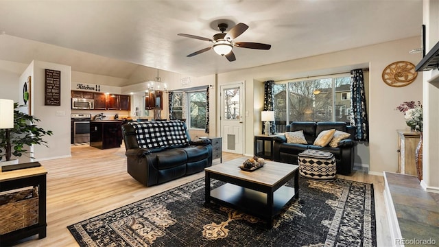 living room with vaulted ceiling, ceiling fan with notable chandelier, light wood-style floors, and baseboards