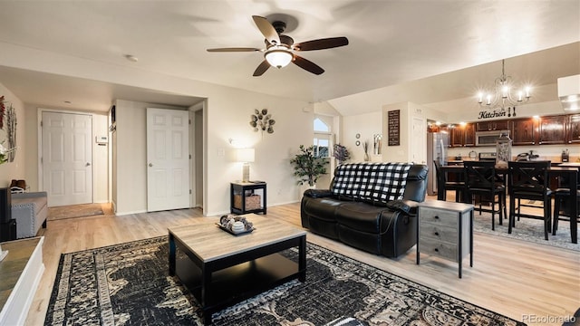 living area with lofted ceiling, ceiling fan with notable chandelier, light wood-type flooring, and baseboards