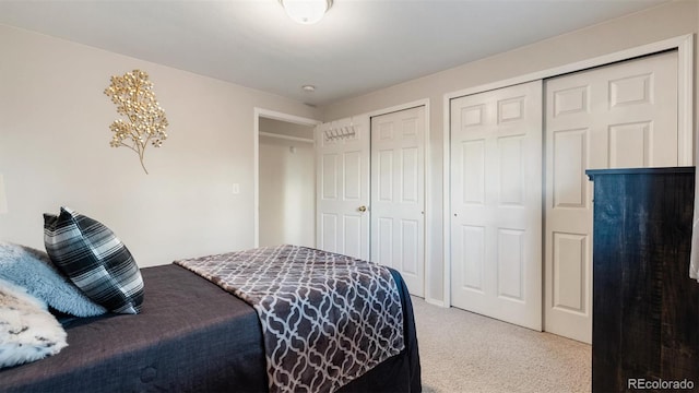 bedroom featuring light colored carpet and two closets