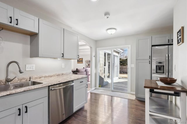 kitchen with baseboards, arched walkways, dark wood-style floors, appliances with stainless steel finishes, and a sink