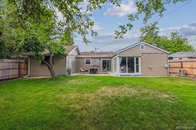 rear view of property with brick siding, fence, a patio, and a lawn