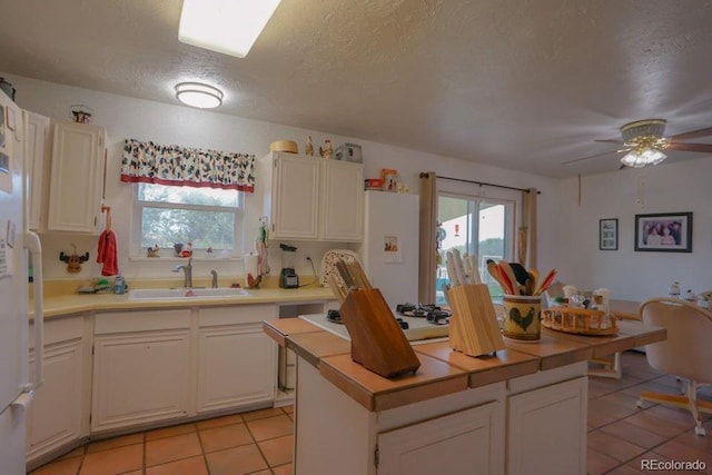 kitchen with ceiling fan, sink, light tile patterned flooring, a textured ceiling, and white cabinets