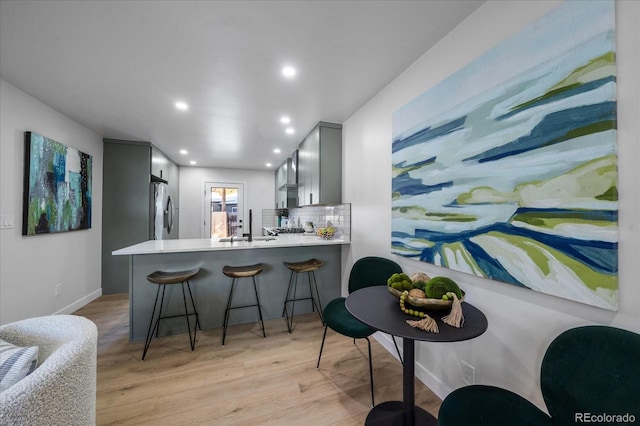 kitchen featuring stainless steel refrigerator, kitchen peninsula, gray cabinets, and light hardwood / wood-style floors