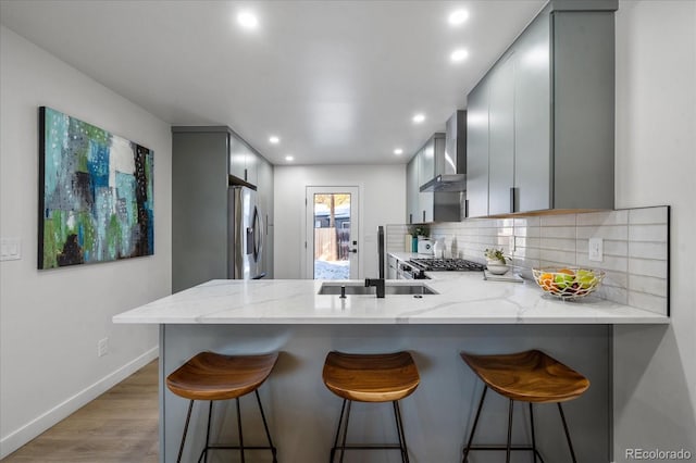 kitchen featuring gray cabinetry, wall chimney exhaust hood, kitchen peninsula, and appliances with stainless steel finishes