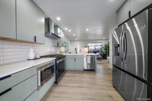 kitchen featuring gray cabinets, light hardwood / wood-style flooring, wall chimney exhaust hood, and stainless steel appliances