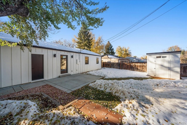 snow covered house featuring a patio area and a storage shed