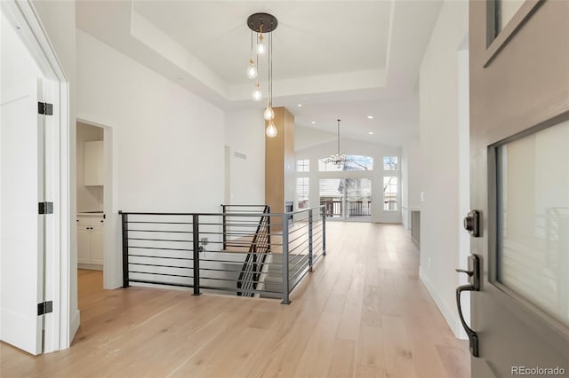 interior space with a notable chandelier, a tray ceiling, a towering ceiling, and light wood-type flooring