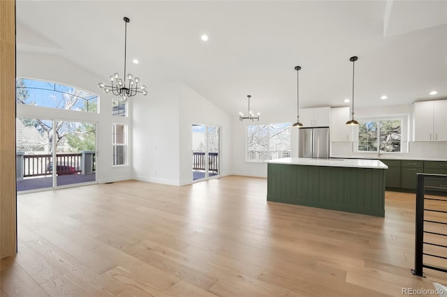 kitchen with white cabinets, a notable chandelier, a kitchen island, and stainless steel fridge