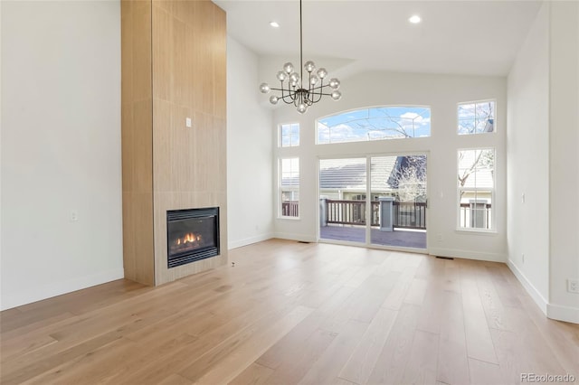 unfurnished living room featuring high vaulted ceiling, a chandelier, light hardwood / wood-style floors, and a tile fireplace