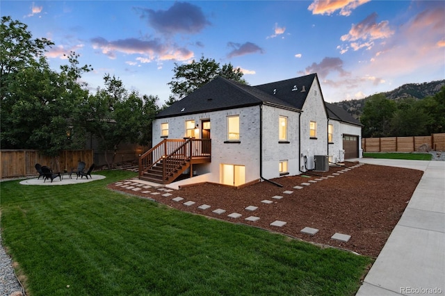 back house at dusk with cooling unit, a patio area, and a lawn