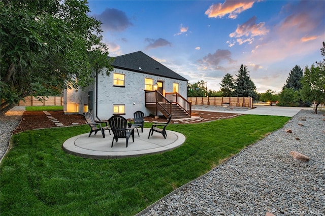 back house at dusk featuring a patio and a lawn