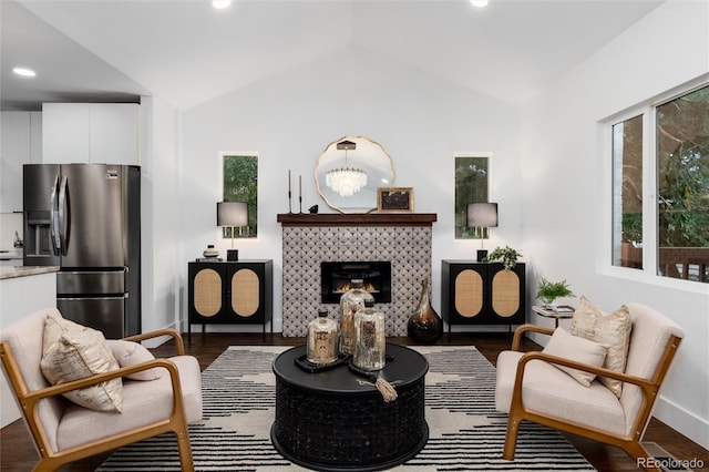 living area featuring a notable chandelier, dark wood-type flooring, vaulted ceiling, and a tile fireplace