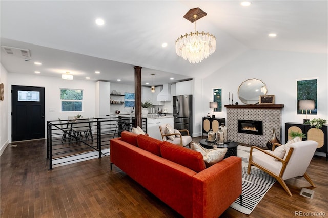 living room featuring a tile fireplace, vaulted ceiling, dark hardwood / wood-style floors, and a notable chandelier