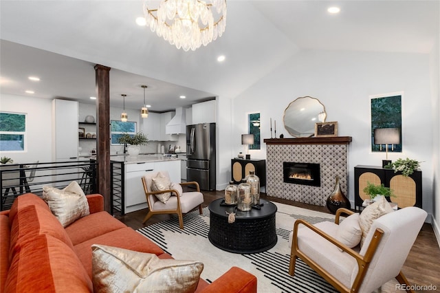 living room featuring a chandelier, wood-type flooring, a tiled fireplace, and vaulted ceiling