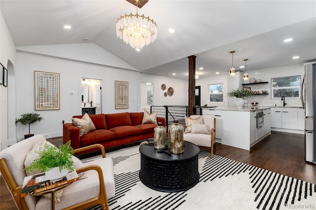 living room with ornate columns, dark hardwood / wood-style floors, lofted ceiling, sink, and a chandelier