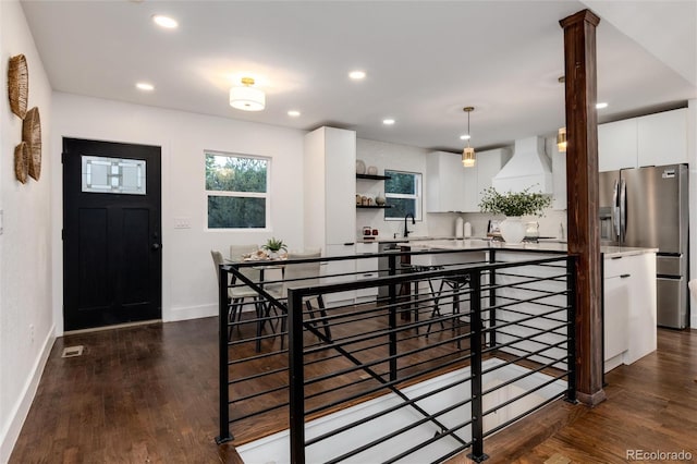 kitchen with dark wood-type flooring, stainless steel refrigerator with ice dispenser, white cabinets, decorative light fixtures, and custom exhaust hood