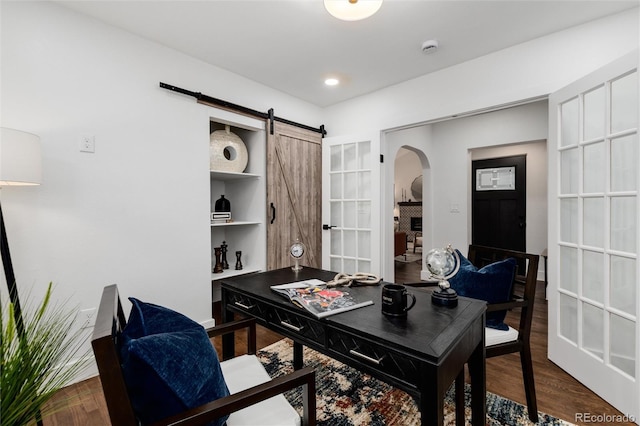 home office featuring wood-type flooring, a barn door, and a fireplace