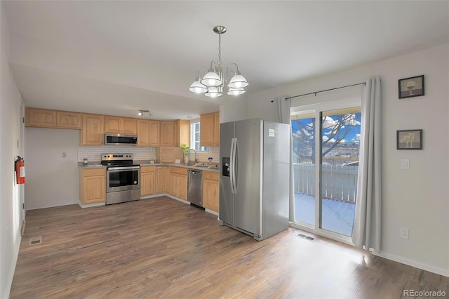 kitchen with light brown cabinets, appliances with stainless steel finishes, a wealth of natural light, pendant lighting, and decorative backsplash