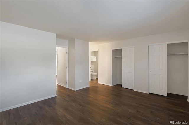 unfurnished bedroom with dark hardwood / wood-style flooring, connected bathroom, and multiple closets