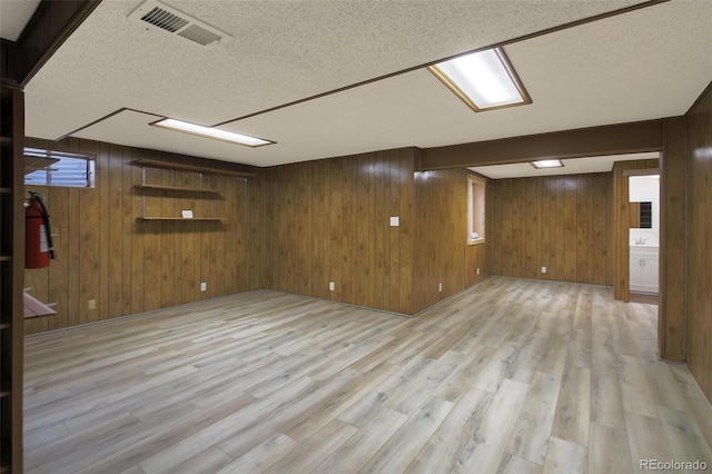 basement with light hardwood / wood-style flooring, a textured ceiling, and wood walls