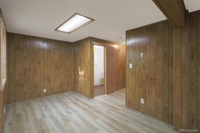 spare room with a textured ceiling, light hardwood / wood-style flooring, and wood walls