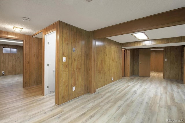 basement with light wood-type flooring, a textured ceiling, and wood walls