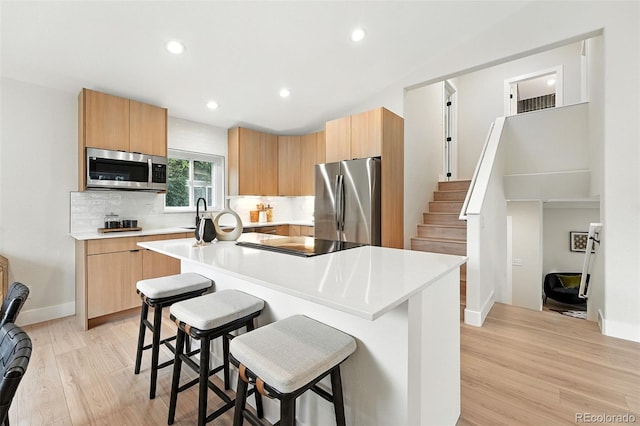 11635 W Security Ave, Lakewood, CO 80401 - kitchen with appliances with stainless steel finishes, a kitchen breakfast bar, light wood-style flooring, light countertops, and a kitchen island