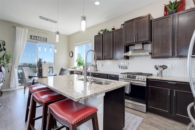 kitchen featuring a sink, wall chimney range hood, gas range, and tasteful backsplash