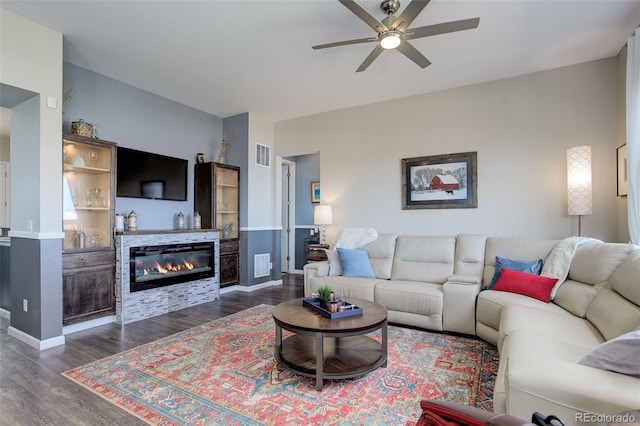 living room featuring a ceiling fan, visible vents, dark wood-style floors, and a glass covered fireplace