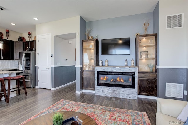 living room featuring visible vents, dark wood-style flooring, a glass covered fireplace, and baseboards