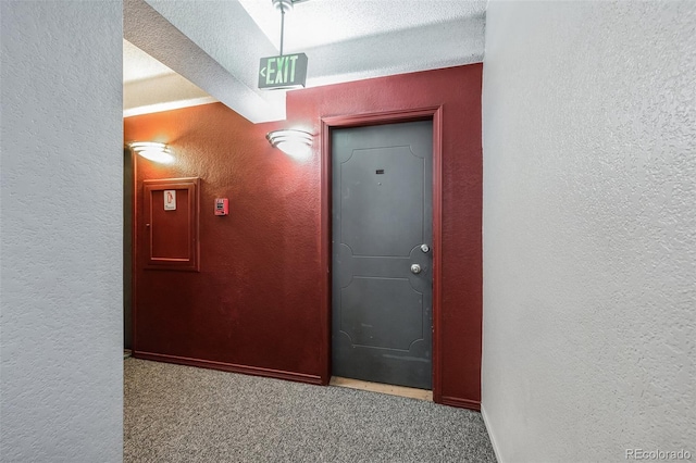 hallway with carpet flooring, a textured ceiling, and a textured wall