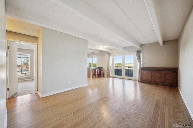 unfurnished living room featuring baseboards, light wood-type flooring, plenty of natural light, and beam ceiling