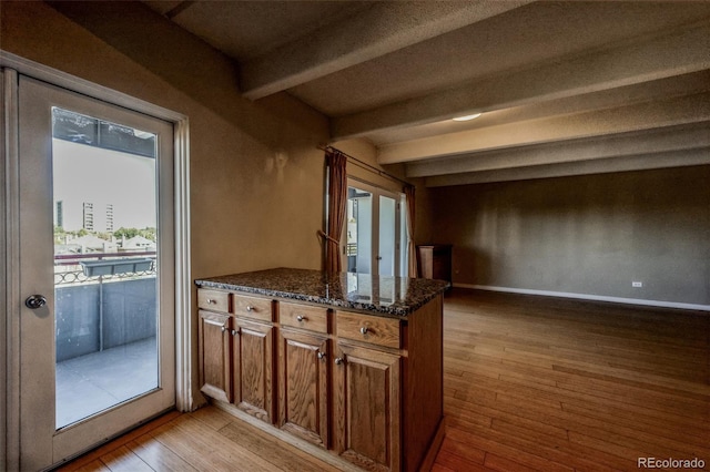 kitchen featuring dark stone countertops, brown cabinetry, baseboards, beam ceiling, and light wood-style floors