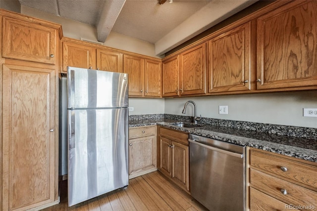 kitchen with dark stone counters, light wood-style flooring, a sink, stainless steel appliances, and brown cabinets