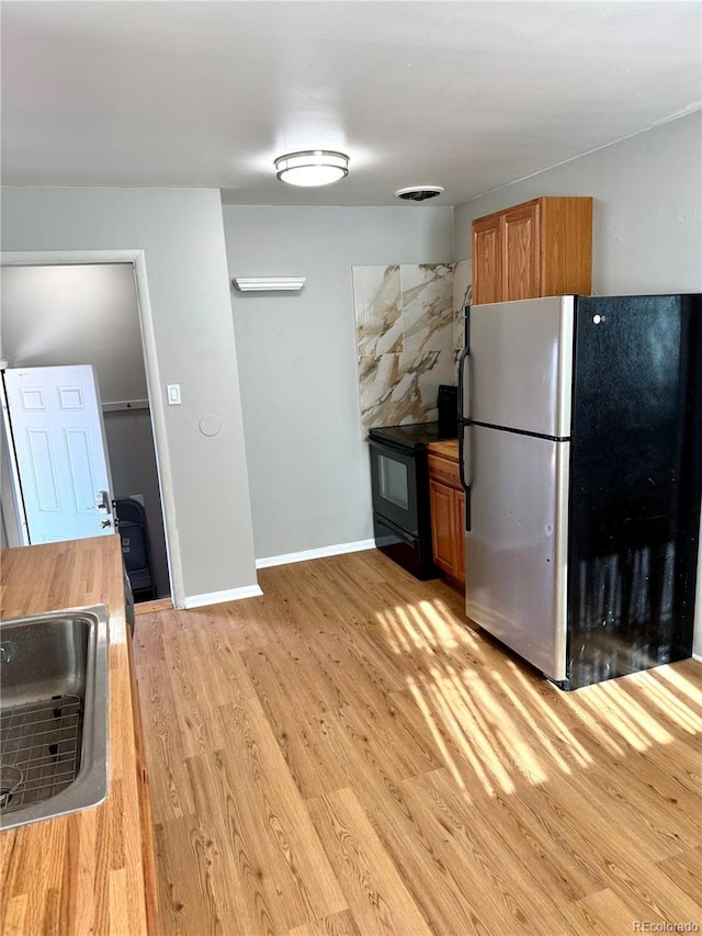 kitchen featuring light hardwood / wood-style flooring, stainless steel fridge, sink, and black electric range