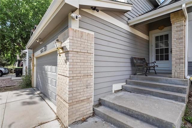 doorway to property featuring an attached garage, concrete driveway, and brick siding