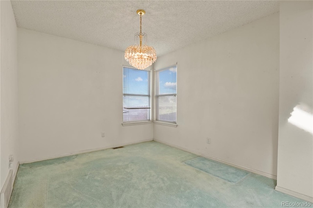 unfurnished room featuring visible vents, light colored carpet, an inviting chandelier, a textured ceiling, and baseboards