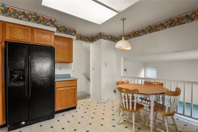 kitchen with pendant lighting, light floors, light countertops, brown cabinetry, and black fridge