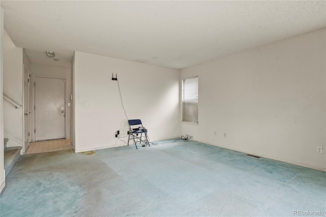 unfurnished room featuring stairs, visible vents, a textured ceiling, and light colored carpet