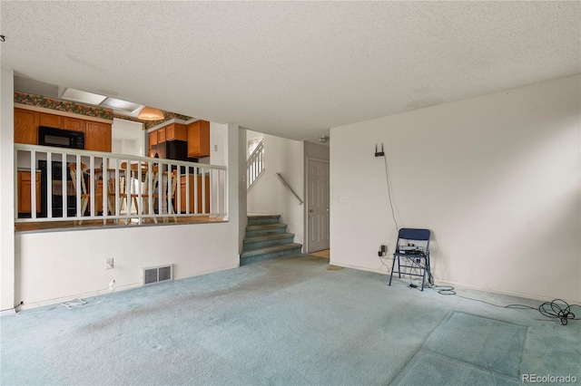 empty room featuring a textured ceiling, stairway, visible vents, and light colored carpet