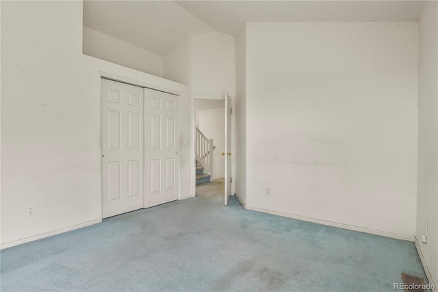 unfurnished bedroom with lofted ceiling, a closet, light colored carpet, and baseboards