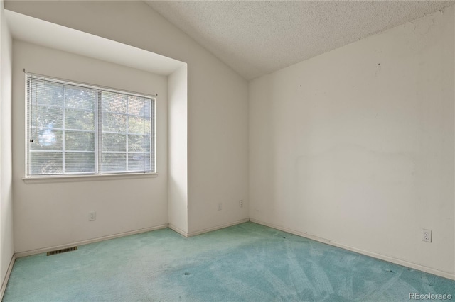 empty room with a textured ceiling, light carpet, visible vents, baseboards, and vaulted ceiling