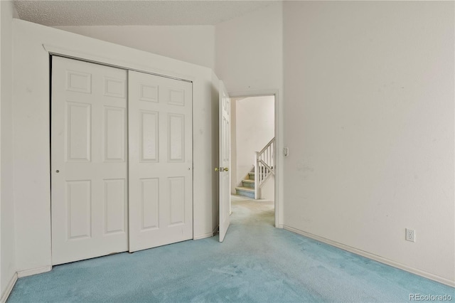 unfurnished bedroom with lofted ceiling, a closet, light carpet, and a textured ceiling