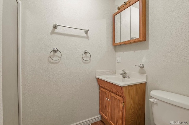 half bath with toilet, a textured wall, and vanity