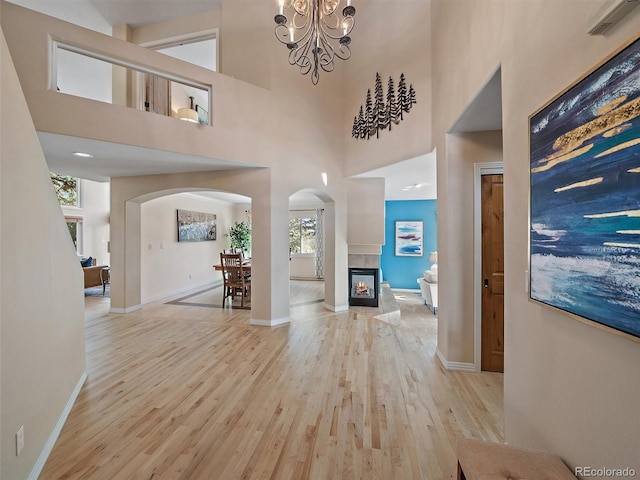 foyer entrance with a tiled fireplace, light hardwood / wood-style floors, a high ceiling, and an inviting chandelier